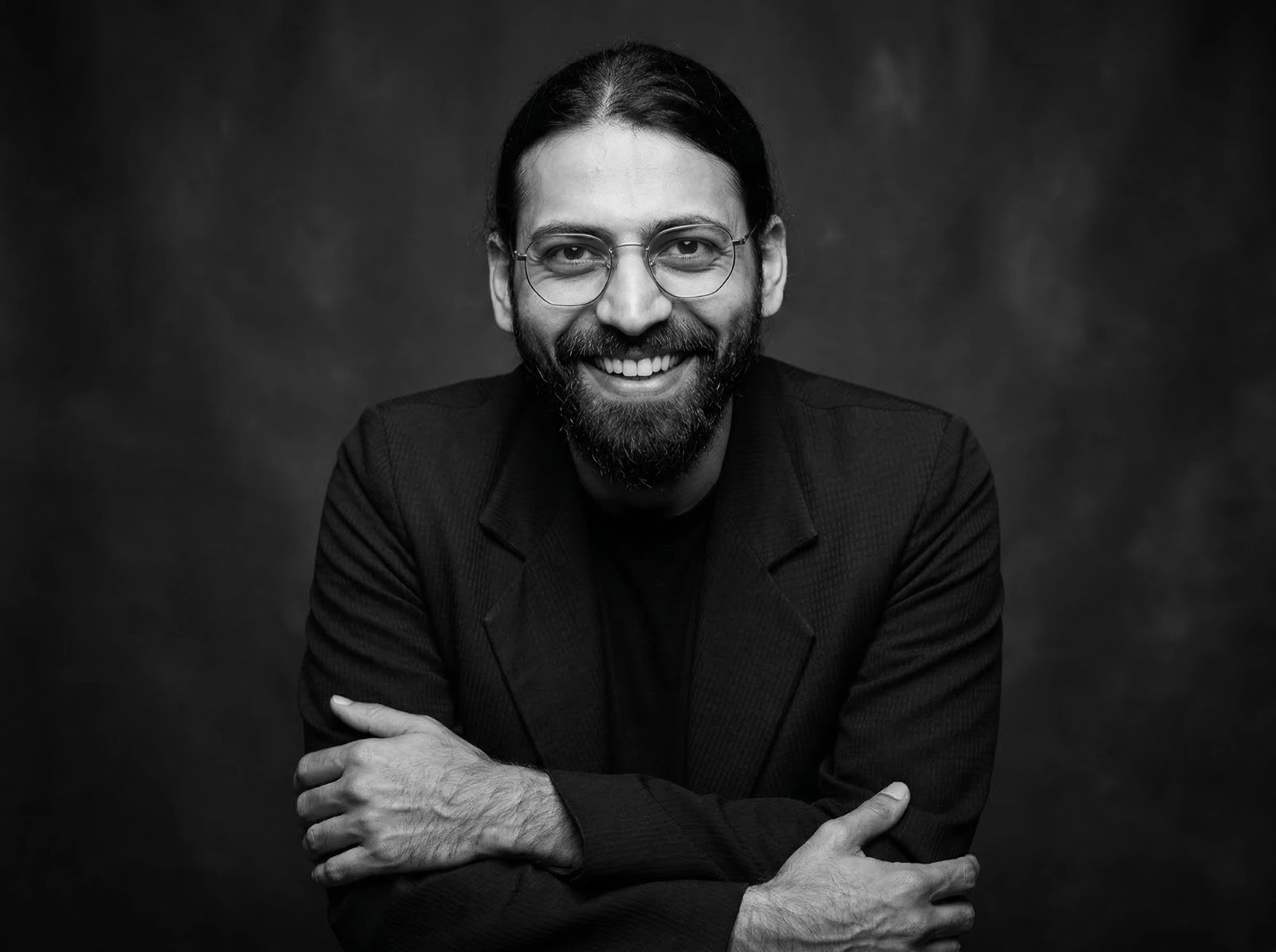 Anurag Tiwari — black and white portrait, smiling, in glasses and a dark jacket with arms folded